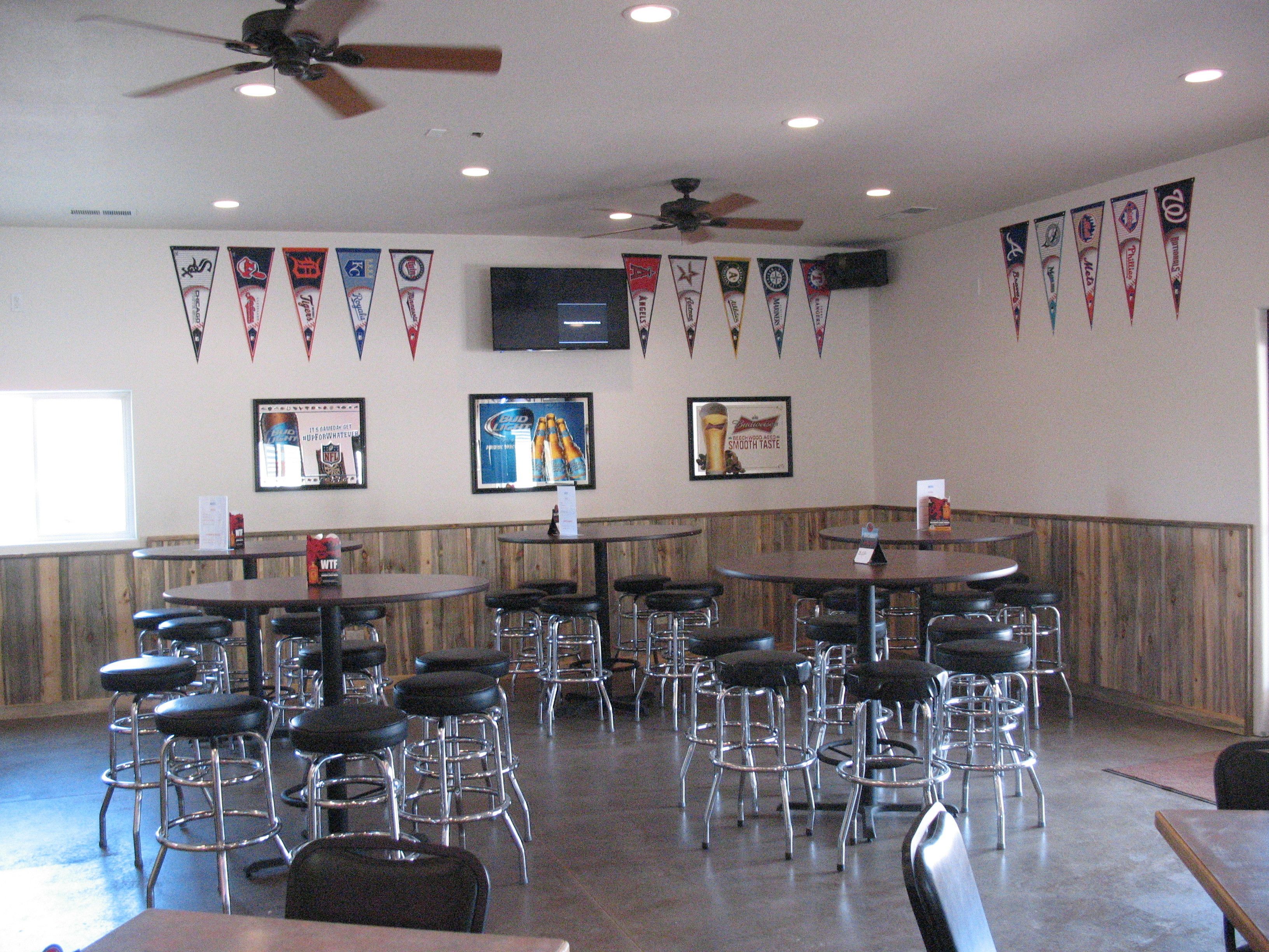 A bar area with multiple tables and stools, ceiling fans, and banners on the walls.