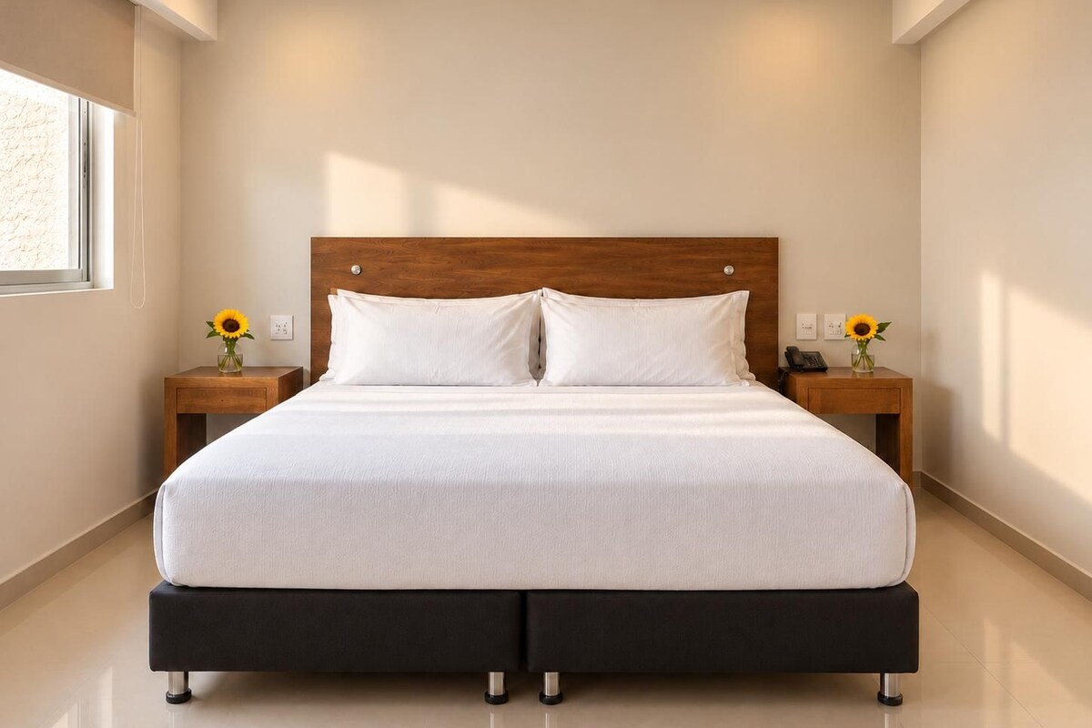 A modern bedroom with a large bed, wooden headboard, two bedside tables with lamps, and a ceiling fan.