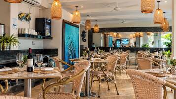 A restaurant with wicker chairs, hanging wicker lamps, and a bar area with a TV screen.