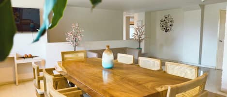 Un comedor con mesa de madera y sillas de mimbre, un jarrón con flores y un adorno en la pared.