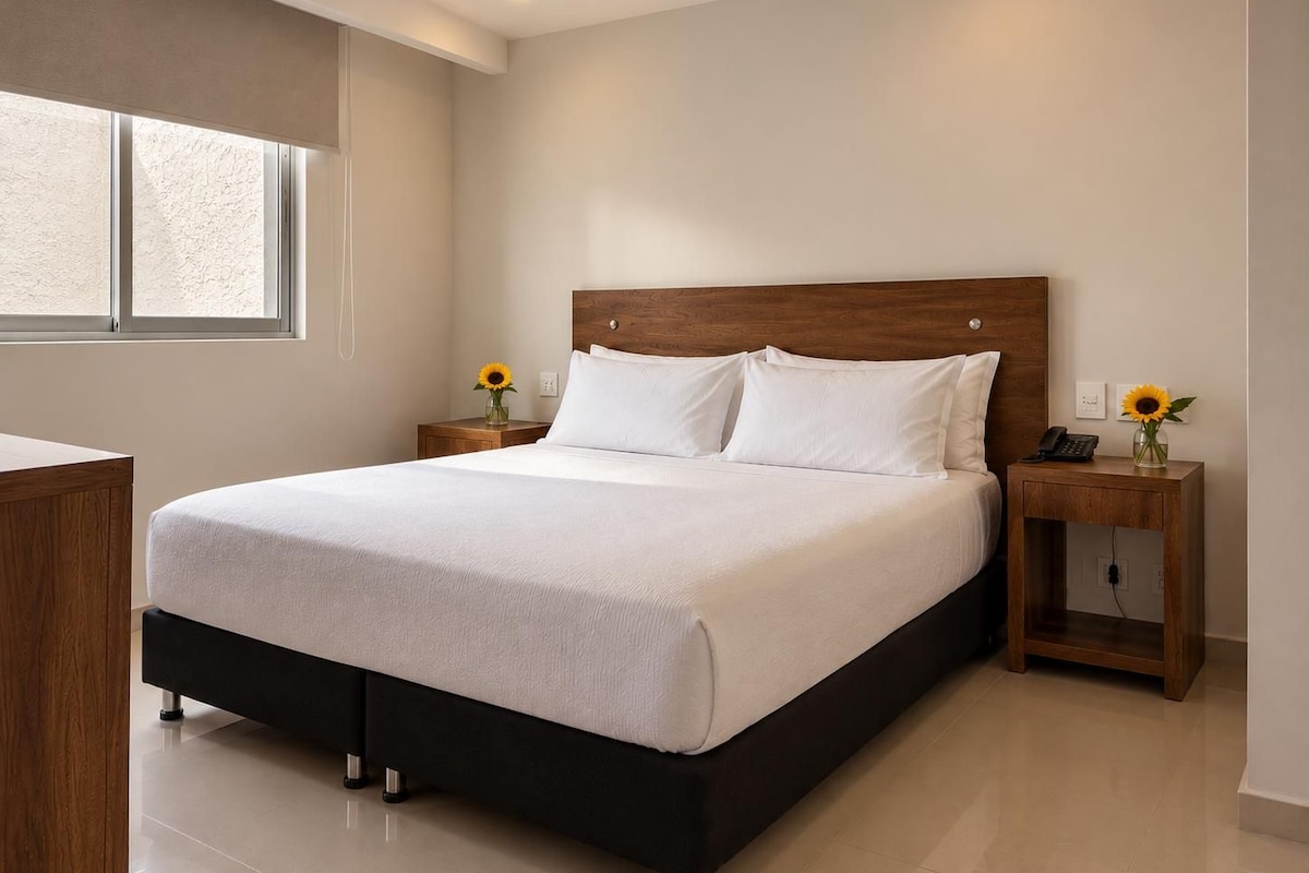 A modern bedroom with a large bed, wooden headboard, and two bedside tables with lamps.