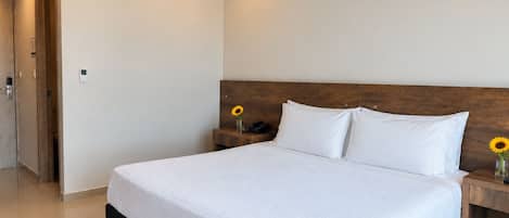Hotellihuone, jossa on sänky, yöpöytä, seinään asennettu ilmastointilaite ja ovi.