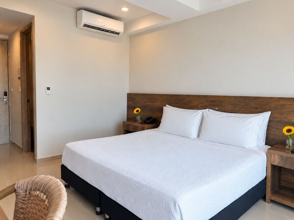 A hotel room with a bed, a nightstand, a wall-mounted air conditioner, and a door.