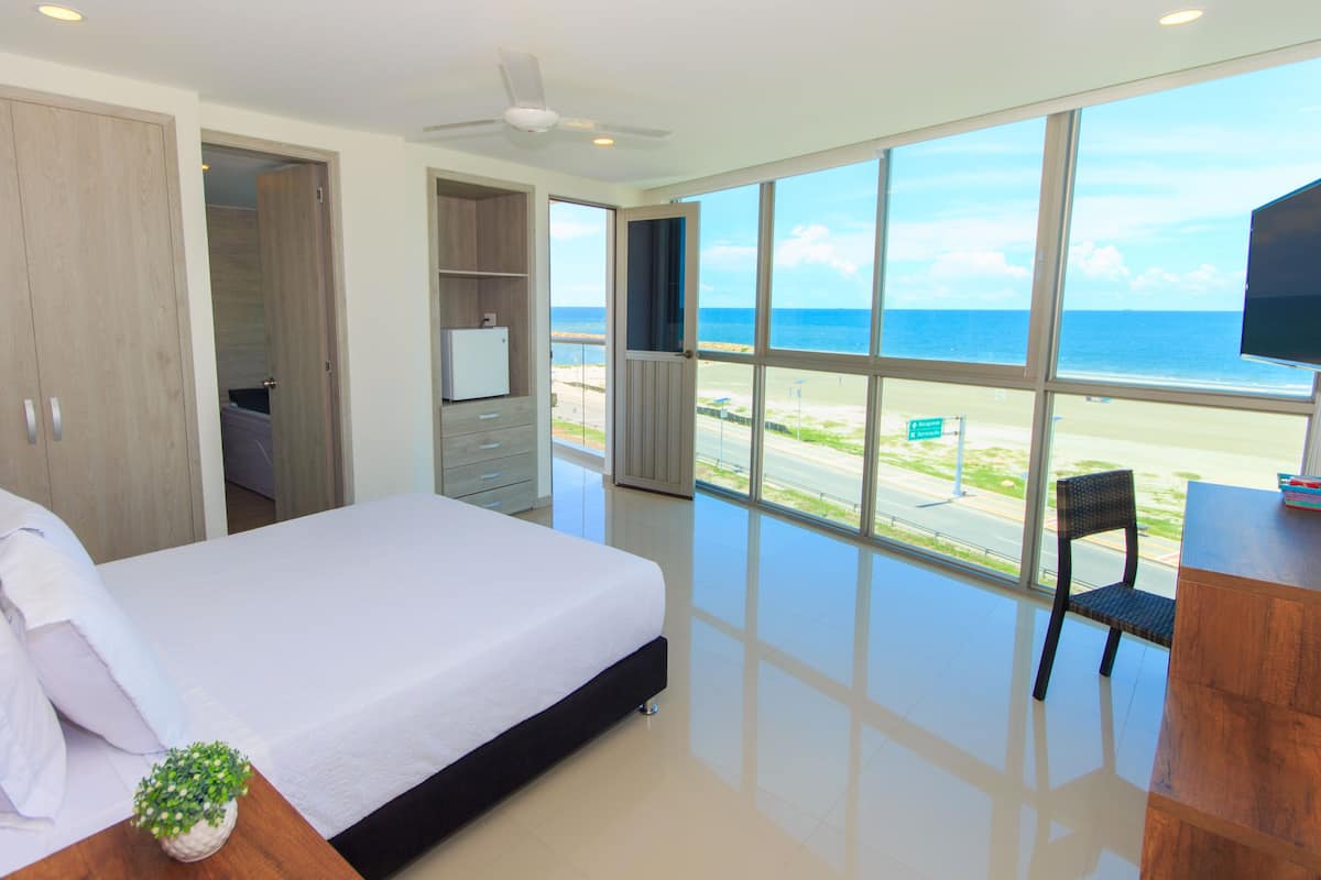 A bedroom with a large bed, a TV, and a view of the beach.