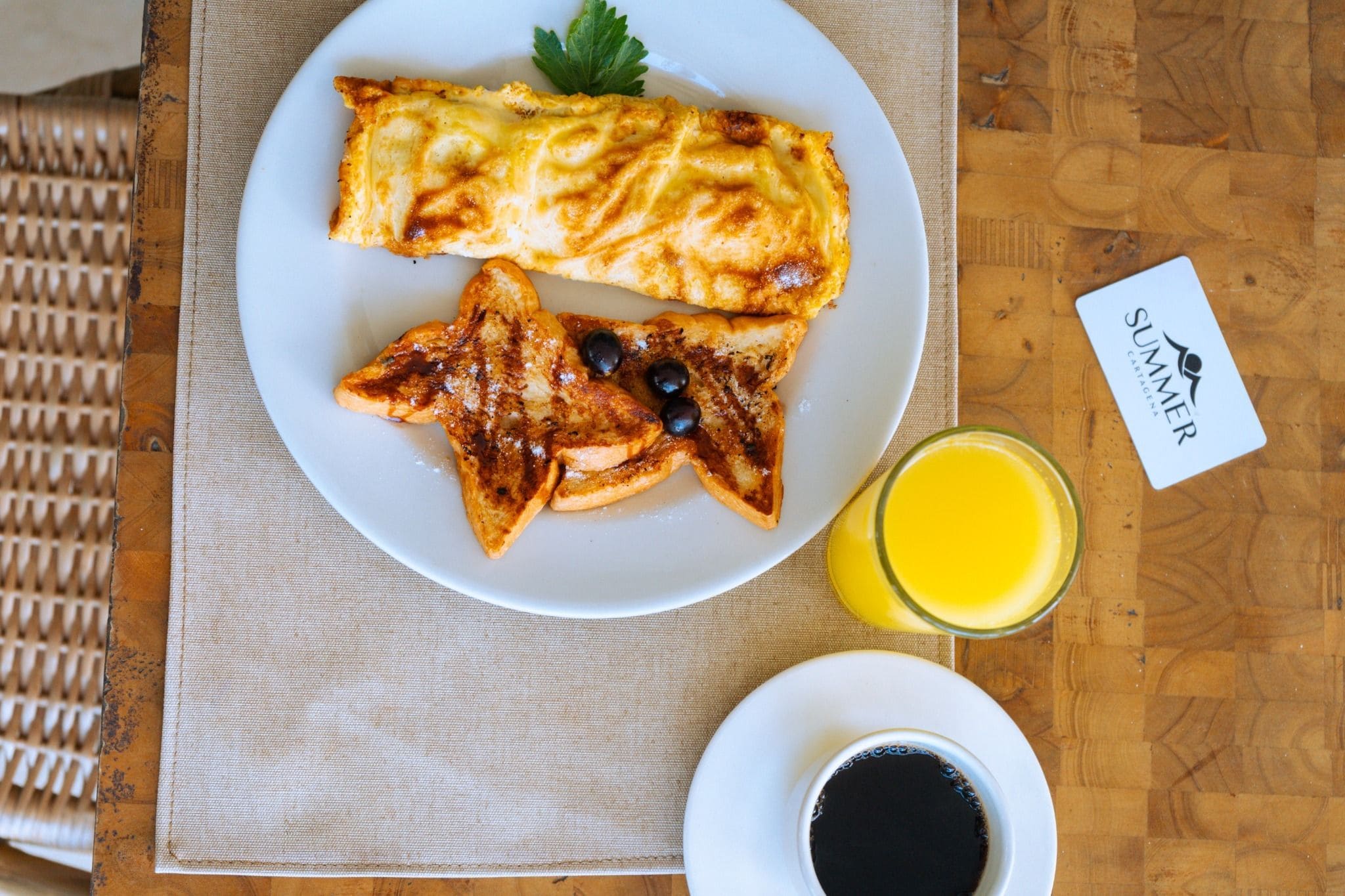 Een ontbijt bord met toast en een omelet, een glas sinaasappelsap en een kop koffie op een houten tafel.
