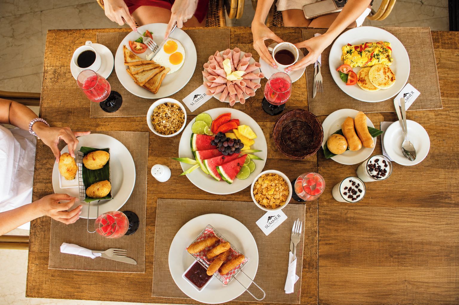 Una mesa de madera con diversos alimentos para el desayuno, como tostadas, huevos, jamón y fruta.