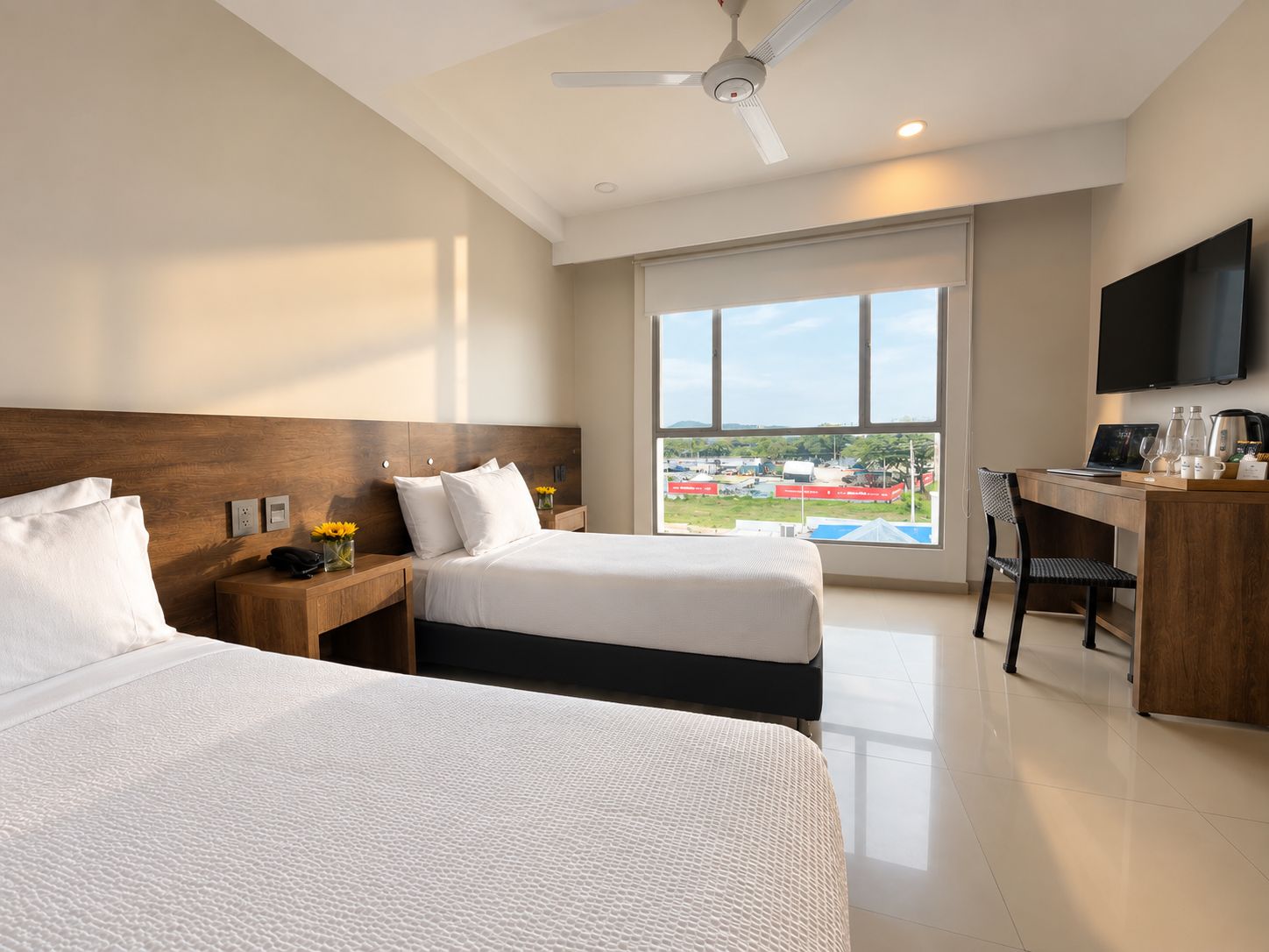 Ein Hotelzimmer mit zwei Betten, einem Schreibtisch, einem Sessel, einem Fernseher und einem großen Fenster mit Blick auf einen Außenbereich.