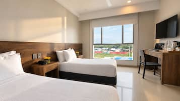 Habitación de hotel con dos camas, un escritorio, una silla, un televisor y un ventanal con vistas a un espacio exterior.