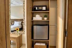 A hotel room with a bed, a mirror, a small table with a vase, a refrigerator, and a shelf with towels and a plant. - Hotel Summer Frente Al Mar (Cartagena)