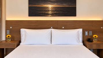 Habitación de hotel con una cama grande, dos mesitas de noche, un cabecero de madera y un cuadro de atardecer en la pared.
