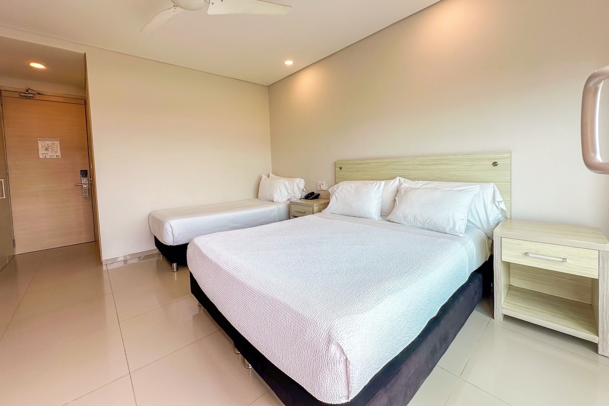 A hotel room with a bed, bedside tables, a ceiling fan, and a door.