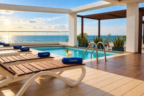 A poolside area with lounge chairs, a pool, and a view of the ocean.