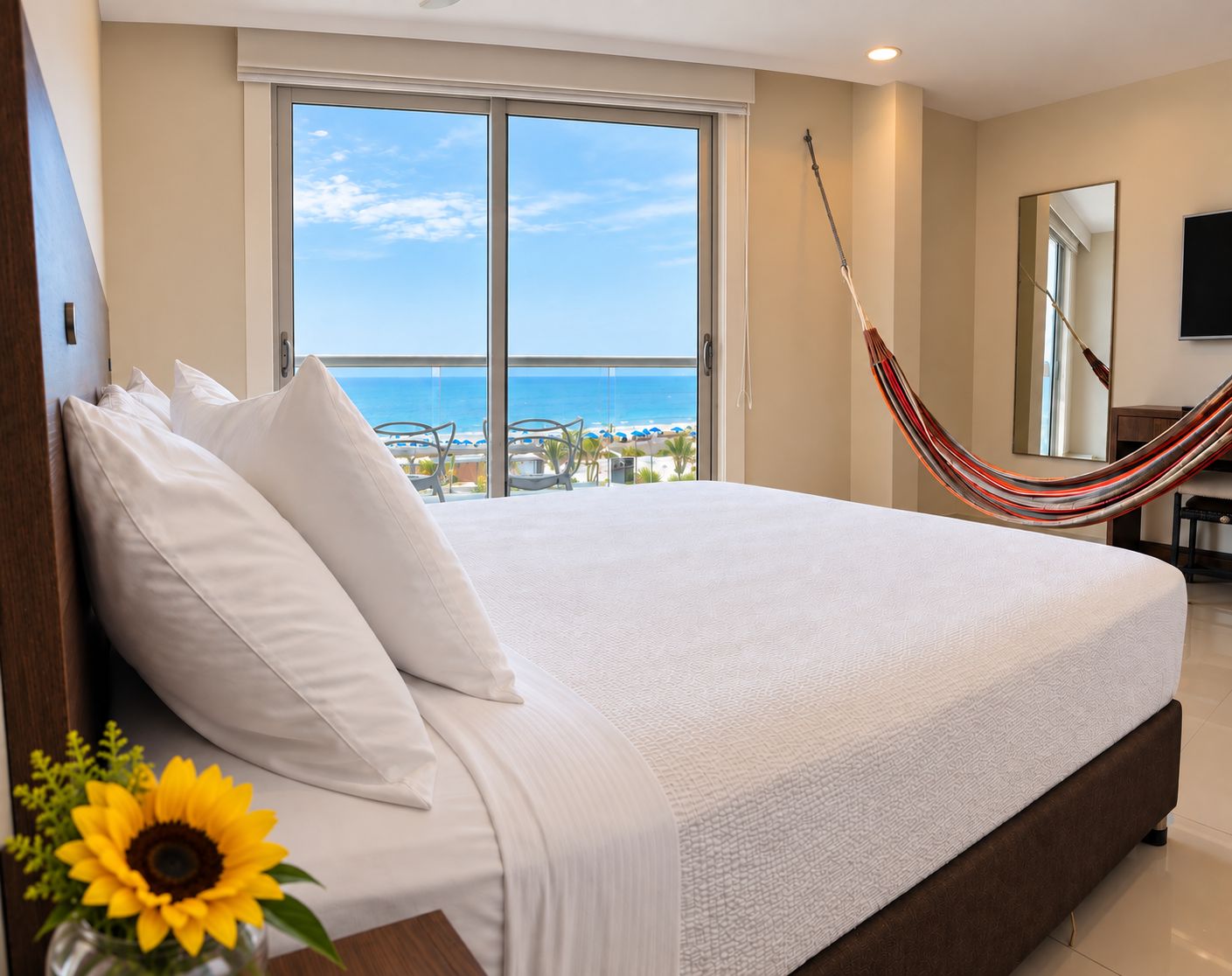 A large bed with white linens, a hammock, and a view of the ocean through a balcony.