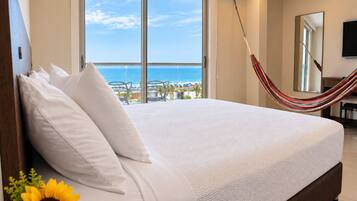 A large bed with white linens, a hammock, and a view of the ocean through a balcony.