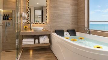 A modern bathroom with a glass-enclosed shower, a large bathtub with sunflowers, and a vanity with a mirror and toiletries.