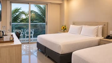 A hotel room with a bed, a desk, a chair, and a balcony with a view of palm trees.