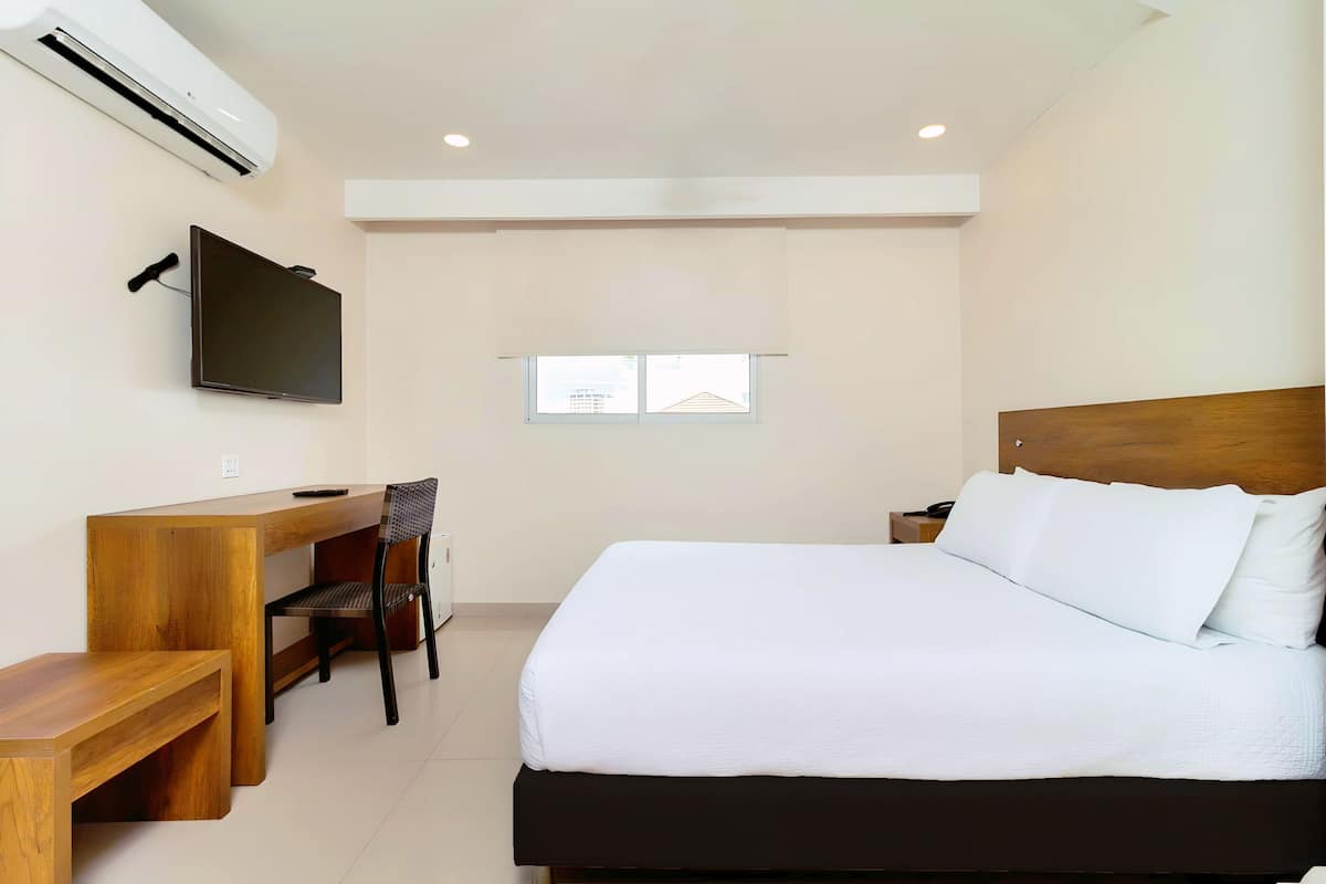A hotel room with a bed, a desk, a chair, a TV, and a window.