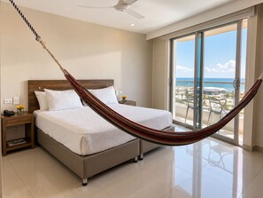 A hotel room with a bed, a nightstand, a telephone, a window with a view of the beach, and a ceiling fan. - Hotel Summer Frente Al Mar (Cartagena)