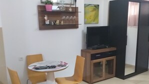 A dining area with a round table and four chairs, a television, a cabinet, and a shelf with decorative items. - Guest House Orlihome (Haifa)