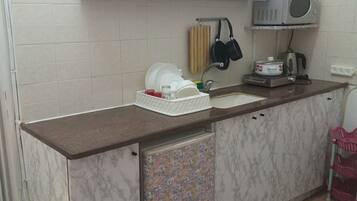 A compact kitchen with a marble countertop, a built-in sink, a microwave, and a small refrigerator.