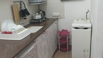 Una cocina compacta con encimera de mármol, microondas, un lavamanos pequeño y refrigerador.
