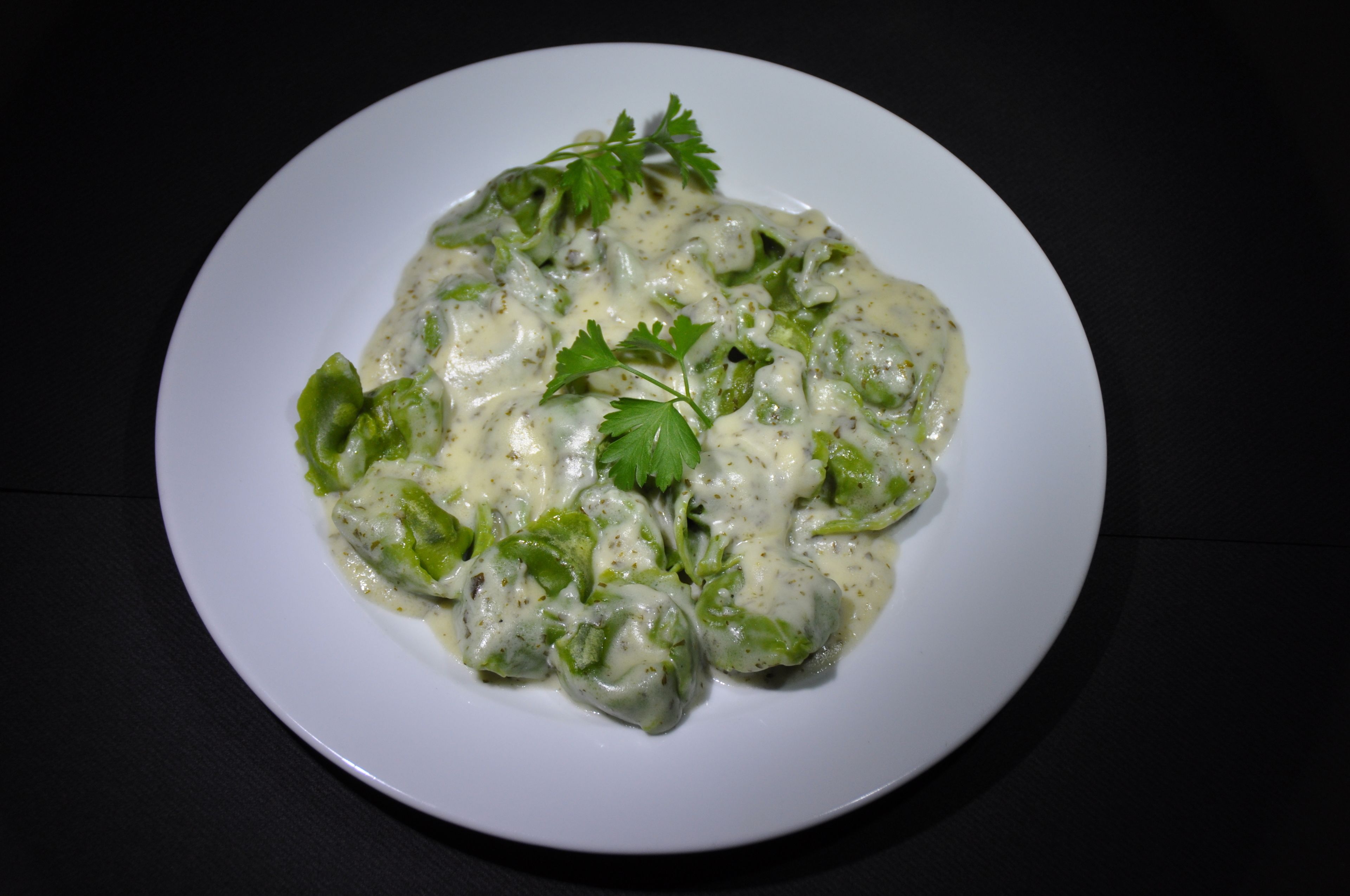 Un plato blanco con un guiso cremoso adornado con perejil, sobre una superficie oscura.