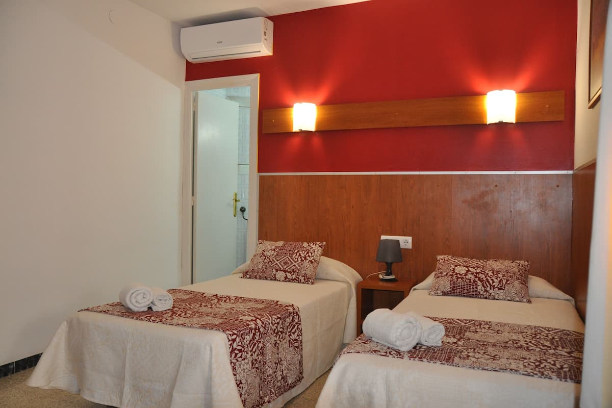 Une chambre d’hôtel avec deux lits, chacun recouvert d’une couvre-lit à motifs et agrémenté d’oreillers, une table de chevet avec une lampe et un appareil de climatisation fixé au mur.
