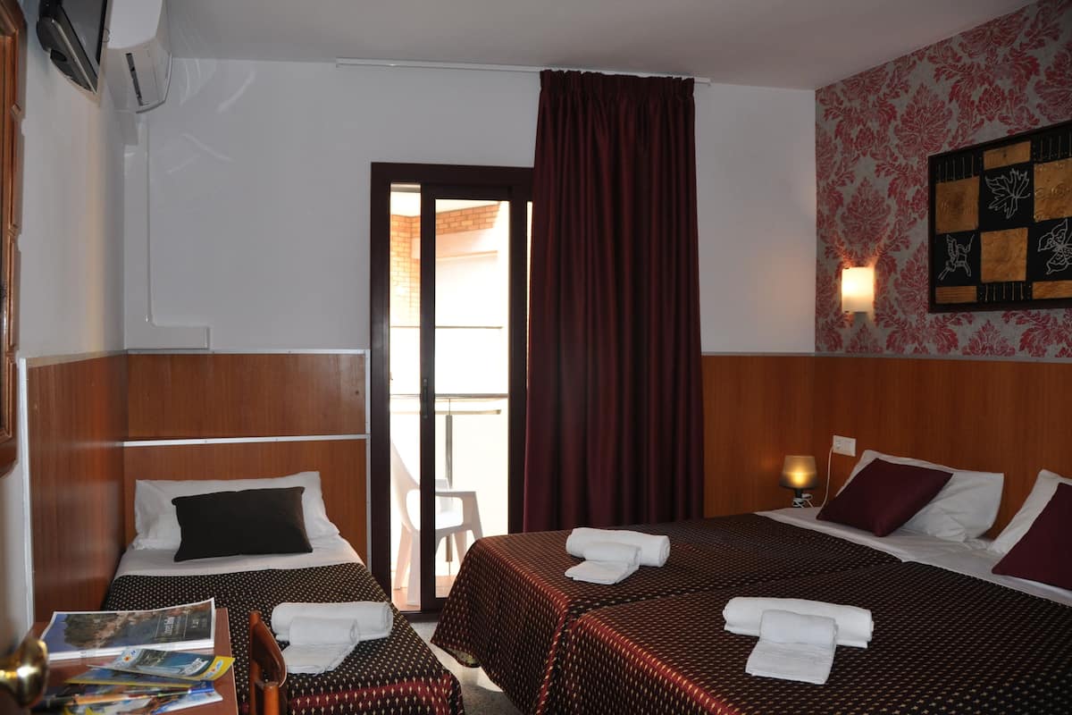 Une chambre d’hôtel avec deux lits, une tête de lit en bois, une petite table avec une chaise, une lampe fixée au mur et une porte donnant sur un balcon.