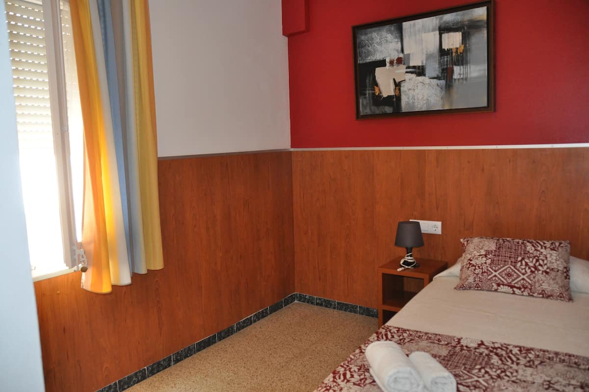 Une chambre d’hôtel avec des boiseries, un lit avec une literie à motifs, une table de chevet avec une lampe et un tableau au mur.