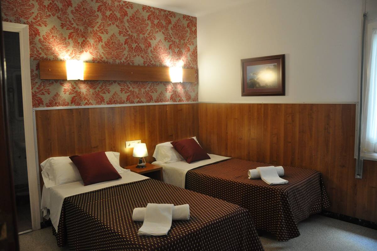 Une chambre d’hôtel avec deux lits, des lambris en bois, un papier peint à motifs floraux et un tableau encadré au mur.