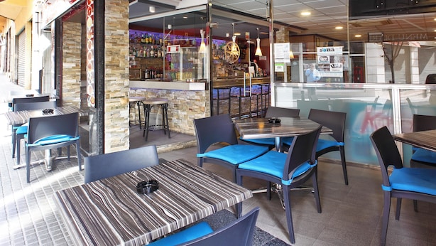 An outdoor cafe with tables and chairs, a bar area, and a stone wall.