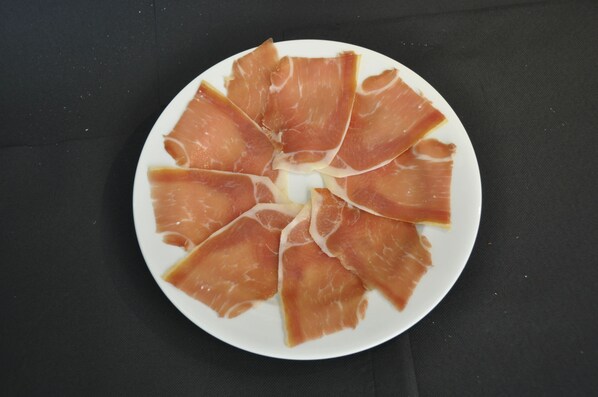 A plate of sliced prosciutto arranged in a circular pattern on a white plate. - Pensión El Amigo (Lloret de Mar)