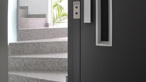 A modern interior with a grey door, a small window, and a staircase leading to a bright room.