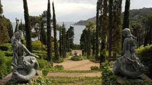 A garden with statues, a pathway, and a view of the sea.