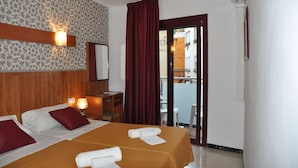 A hotel room with two beds, a wooden headboard, a desk with a chair, a red curtain, and a view of the outside.