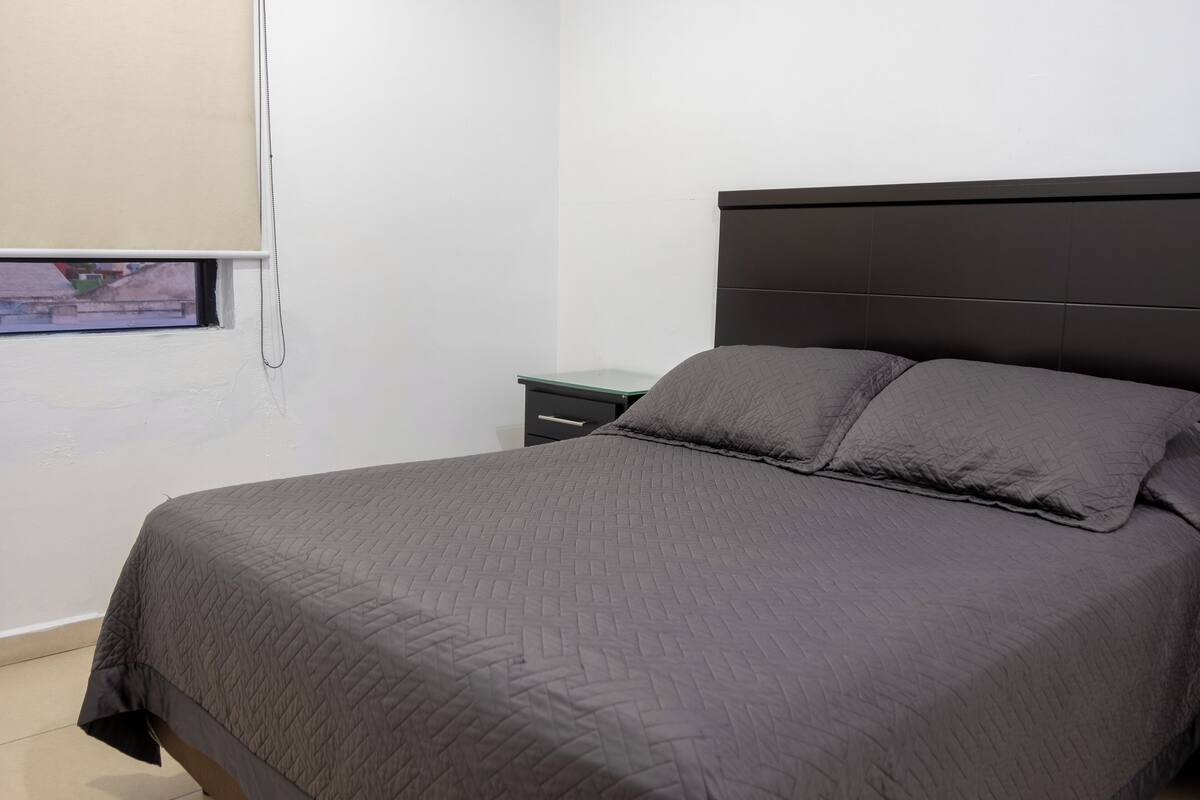 A bedroom with a bed, a nightstand, and a window with blinds.