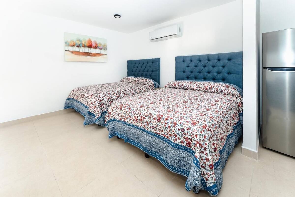 A bedroom with two beds, a large air conditioning unit, and a modern refrigerator.