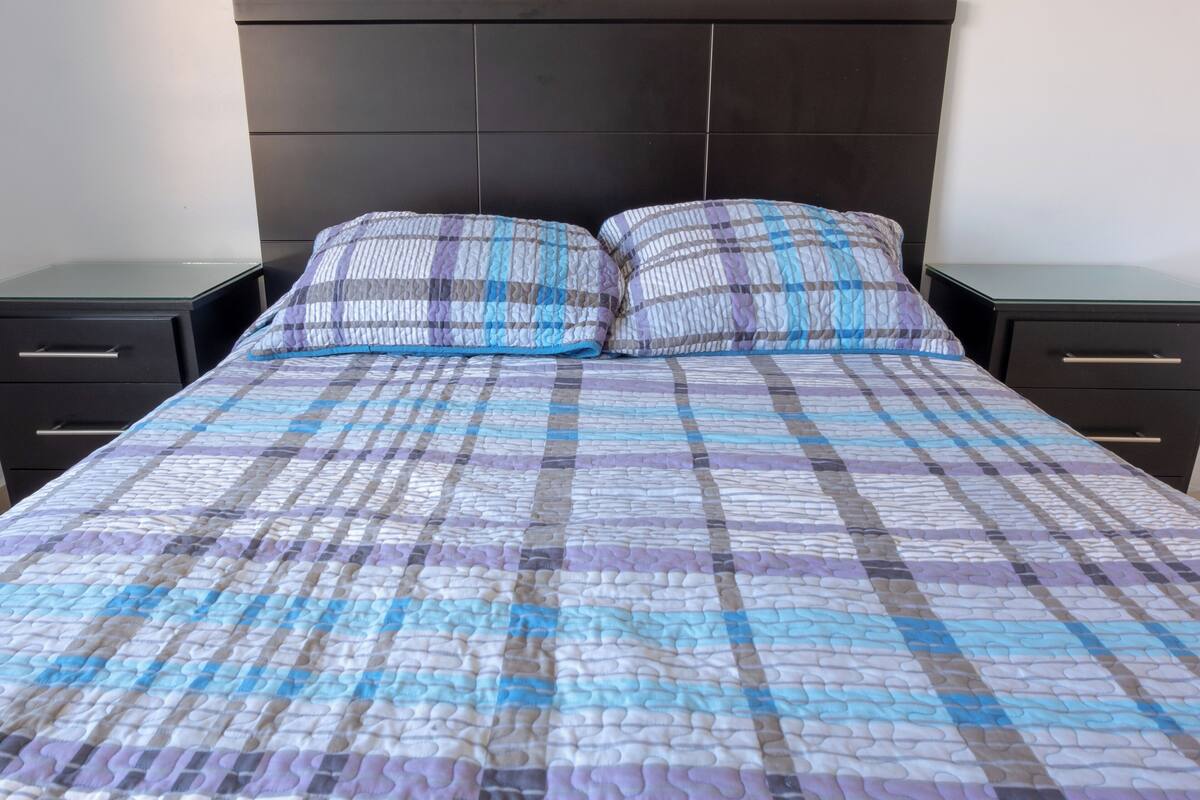 A bed with a checkered quilt, two bedside tables, and a dark headboard.