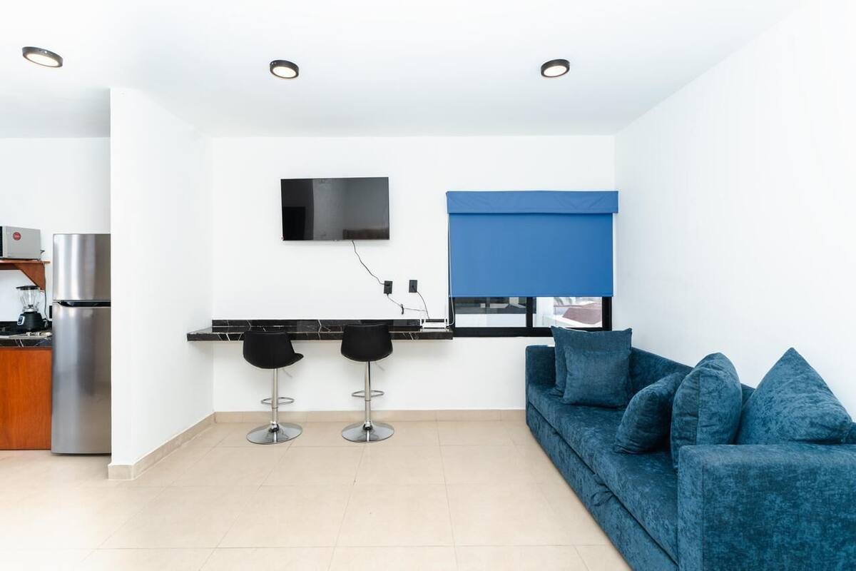 A modern kitchen with a built-in stove, a flat-screen TV mounted on the wall, and a blue window blind.