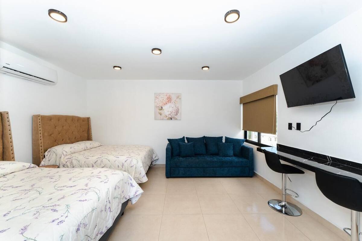 A hotel room with two beds, a sofa, a TV, and a bar area.