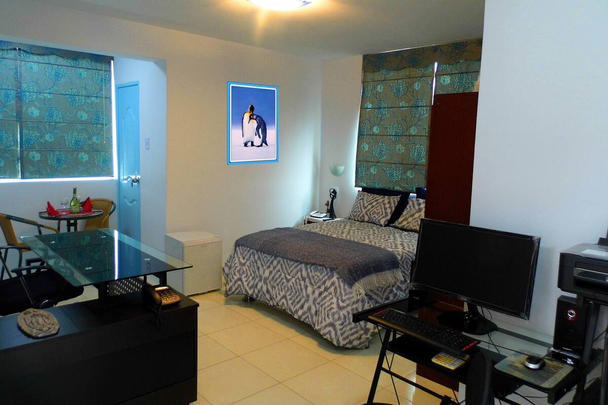 Une chambre à coucher avec un lit, un bureau avec un ordinateur, une chaise, une fenêtre avec des rideaux et un tableau accroché au mur.