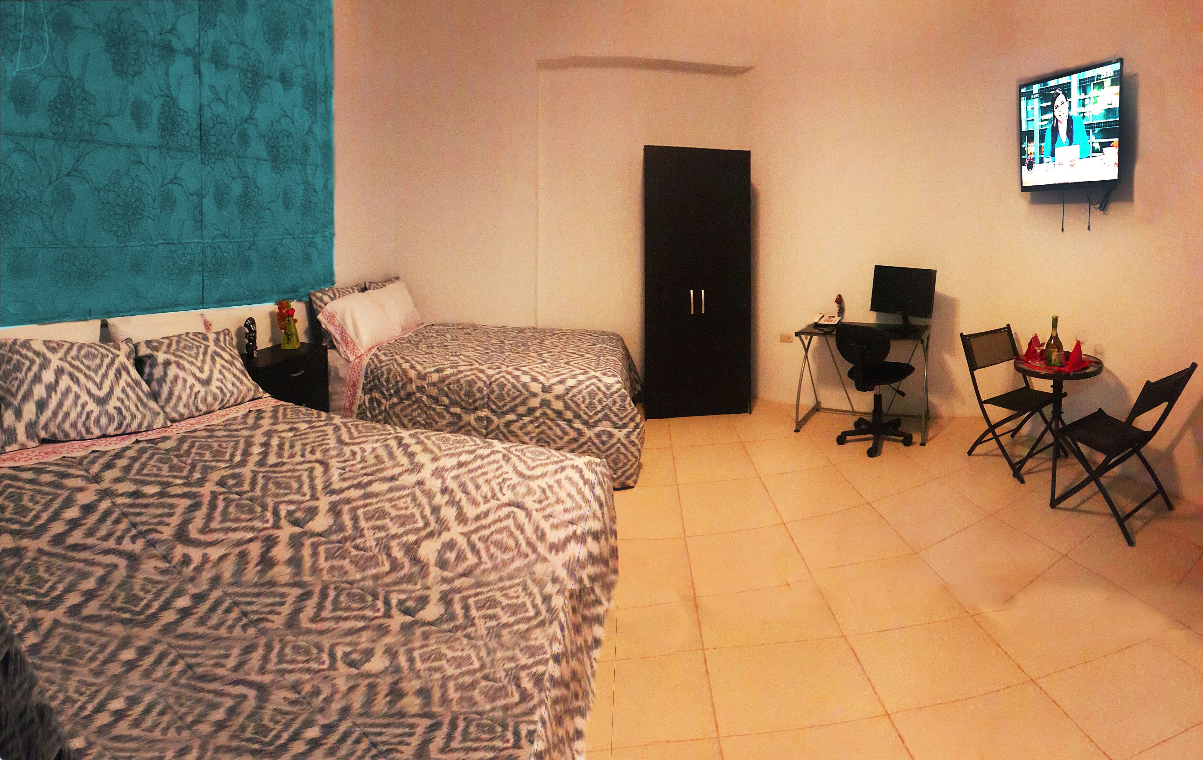 Una habitación de hotel con dos camas estampadas, un escritorio con una computadora y un televisor en la pared.