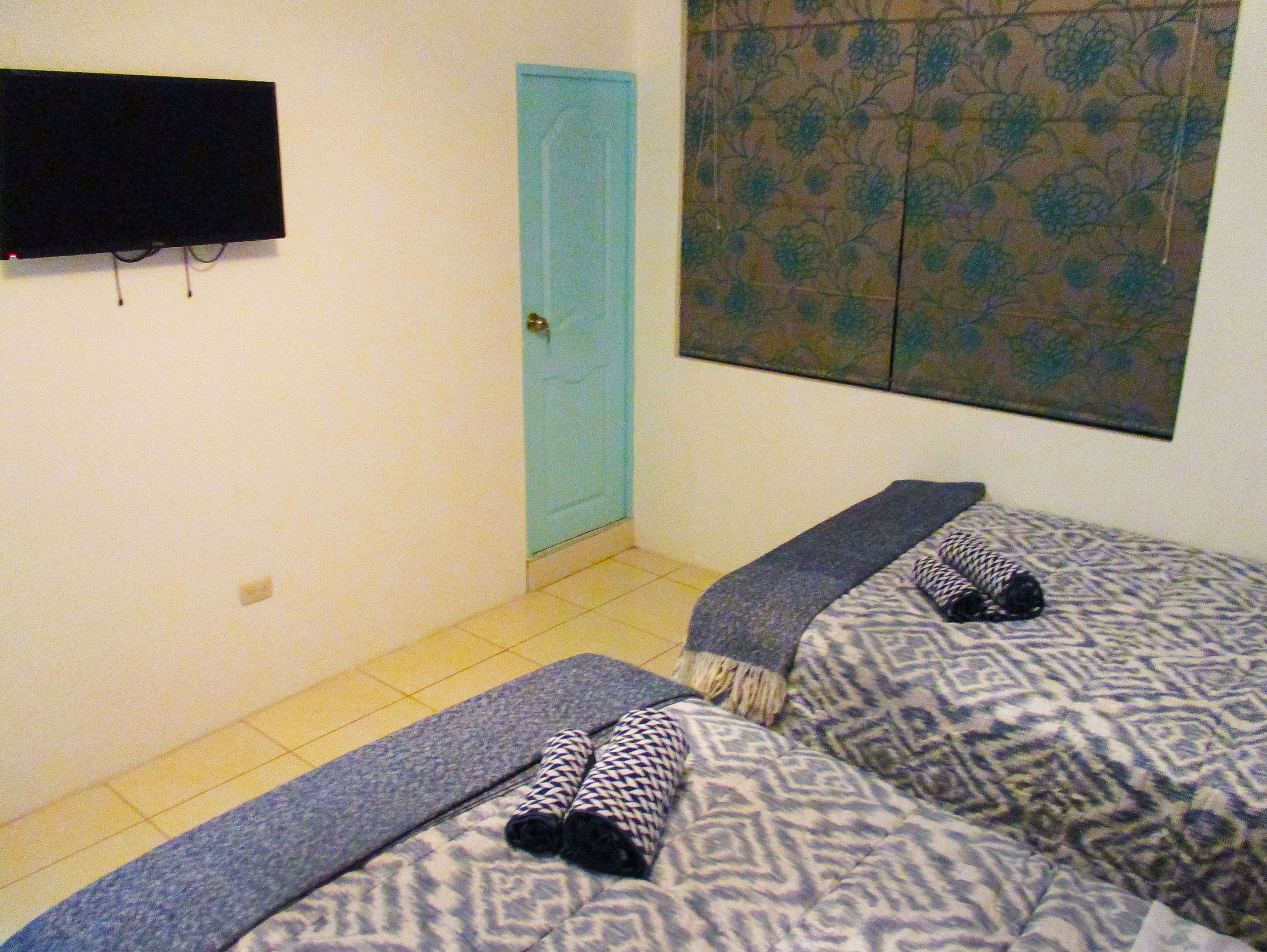 Een kamer met twee bedden, een aan de muur bevestigde televisie, een blauwe deur en een wanddecoratie met een patroon.