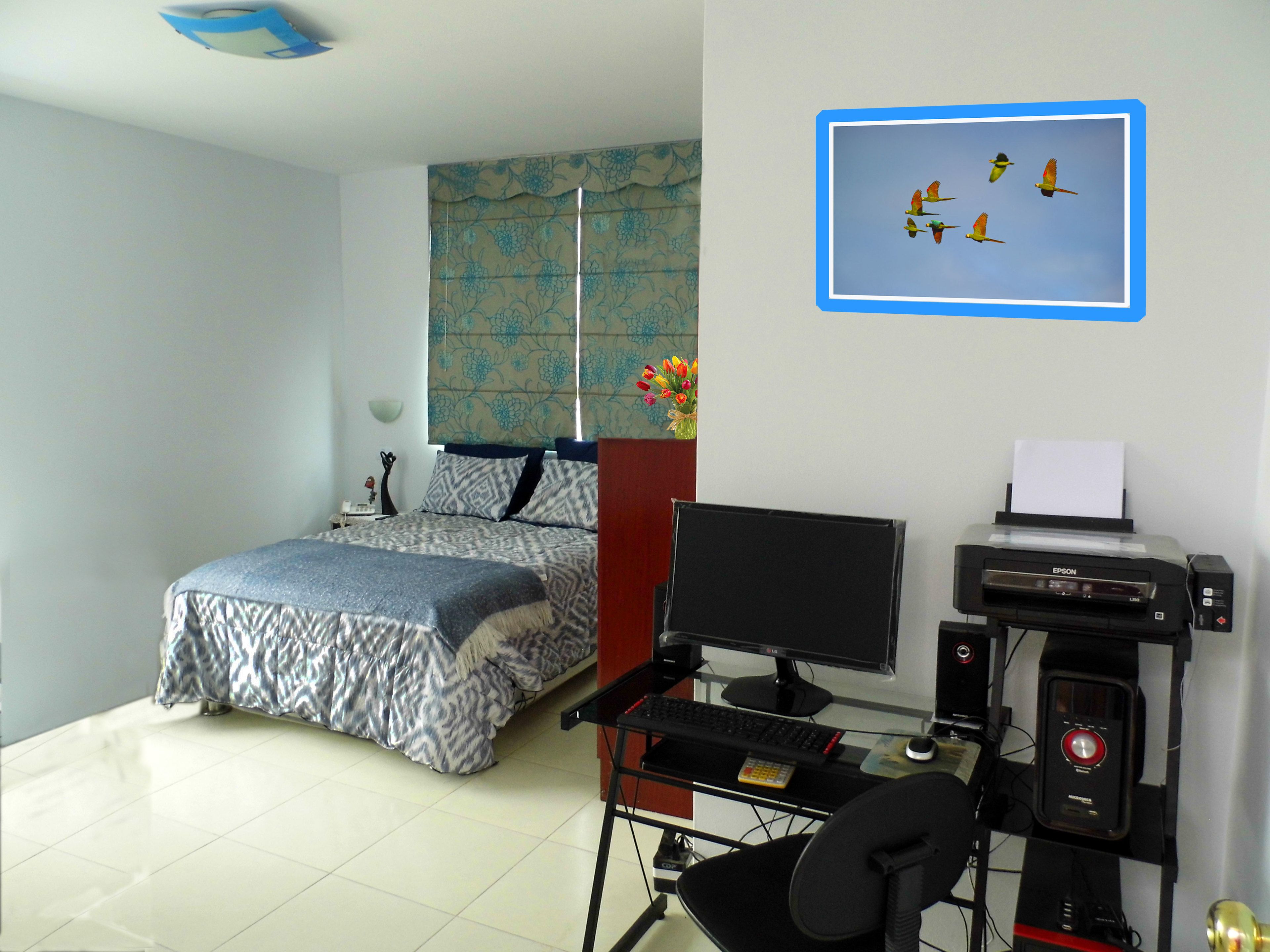 A bedroom with a bed, a desk with a computer, and a printer.