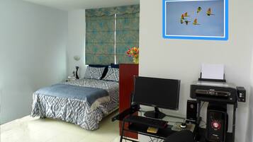 A bedroom with a bed, a desk with a computer, and a printer.