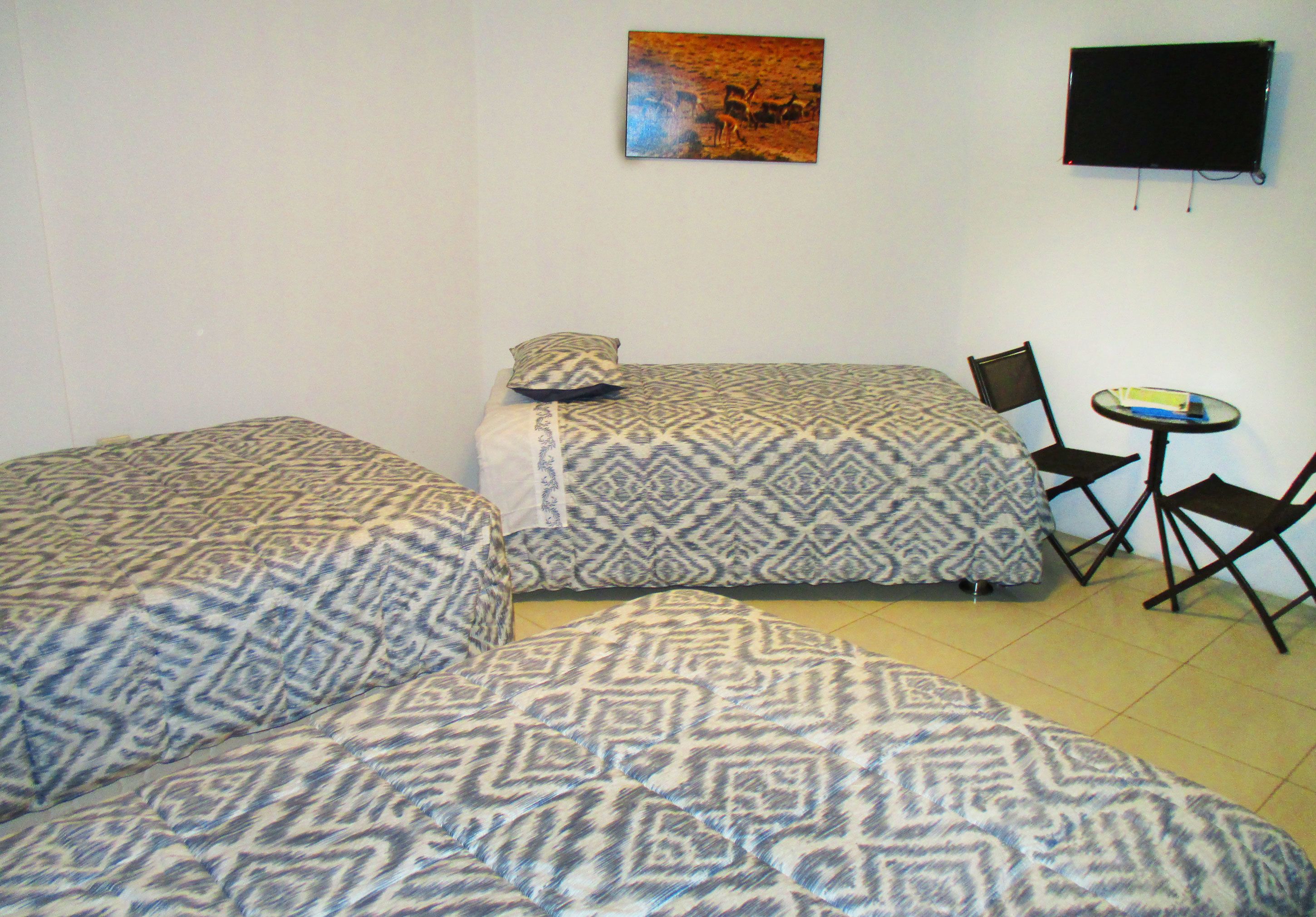 A room with two beds, a small table, and a TV on the wall.