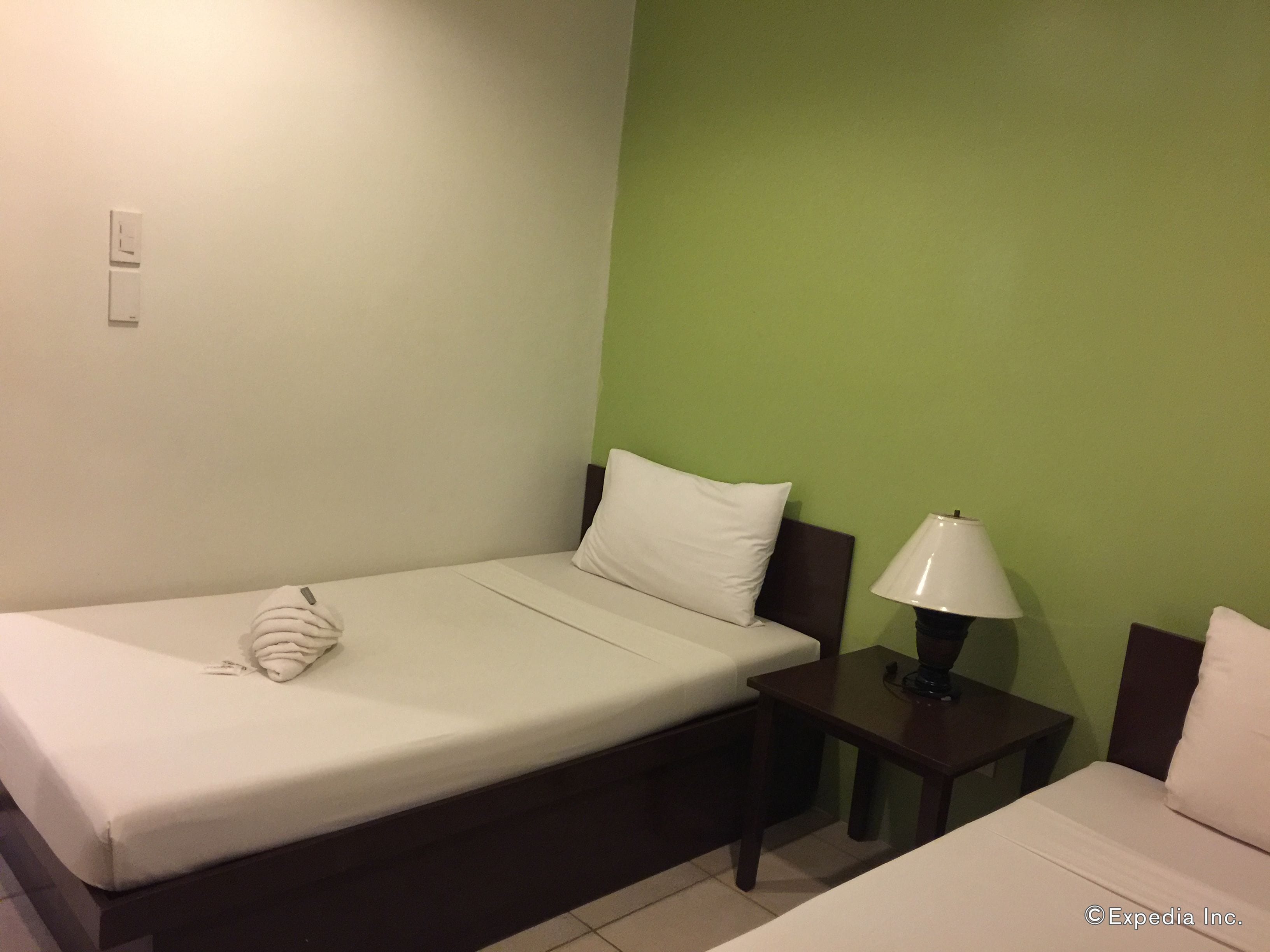 A single bed with a white pillow and a folded blanket, a bedside table with a lamp, and a green wall.