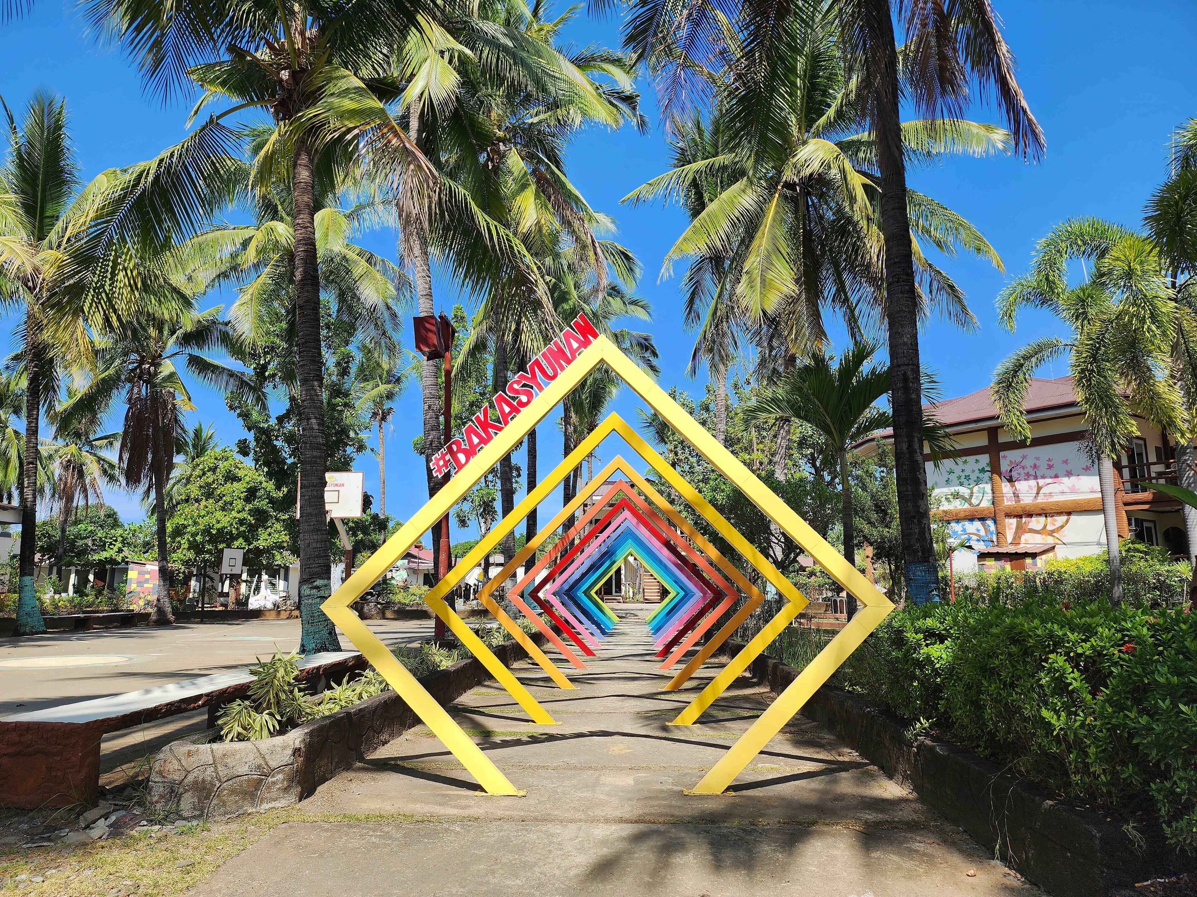 A pathway with colorful geometric shapes leading to a building with a tree mural.