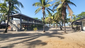A beachfront property with a covered outdoor area, palm trees, and a sandy beach. - Bakasyunan Resort Zambales (Iba)