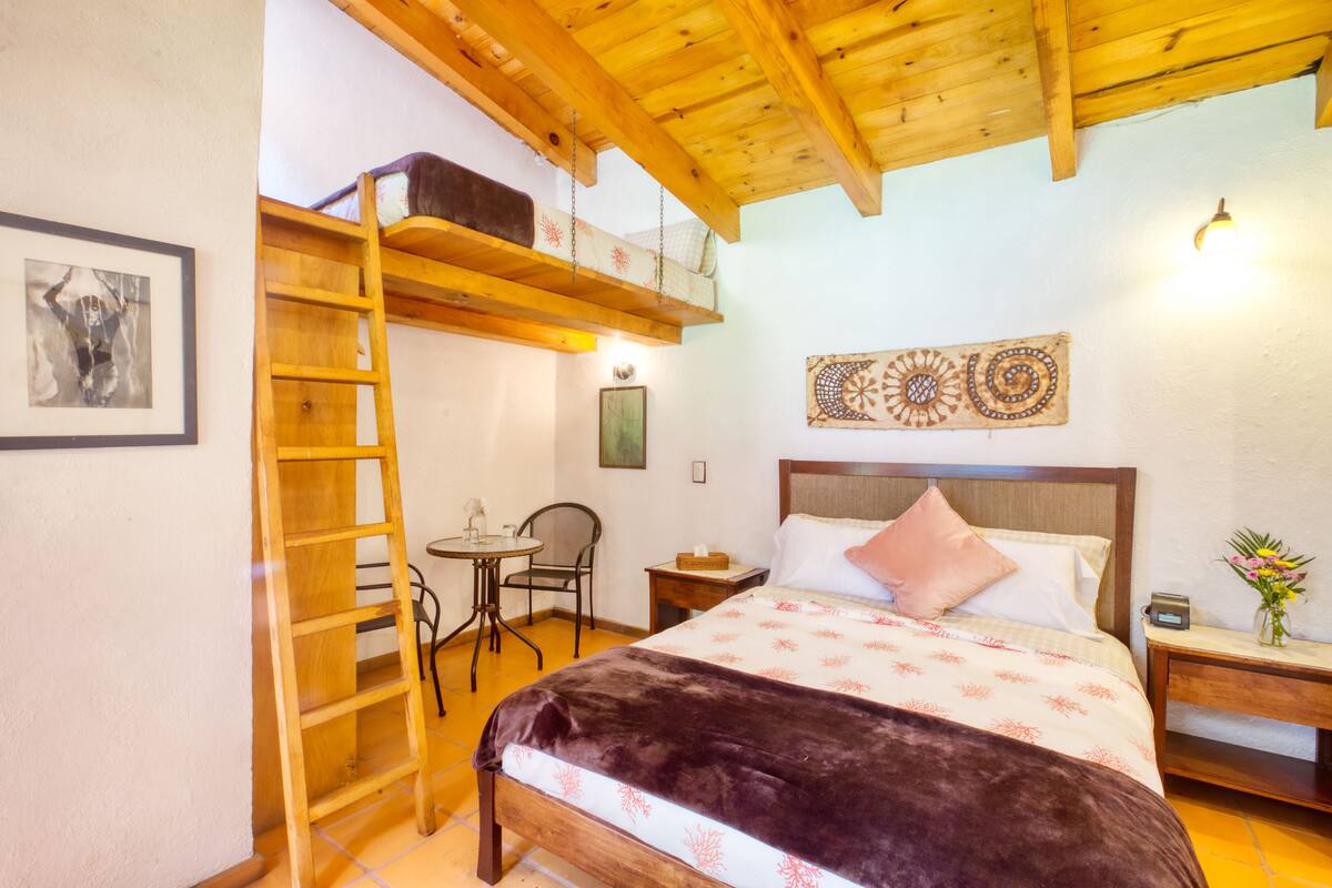A bedroom with a wooden bed, a ladder, a small table, and a chair.